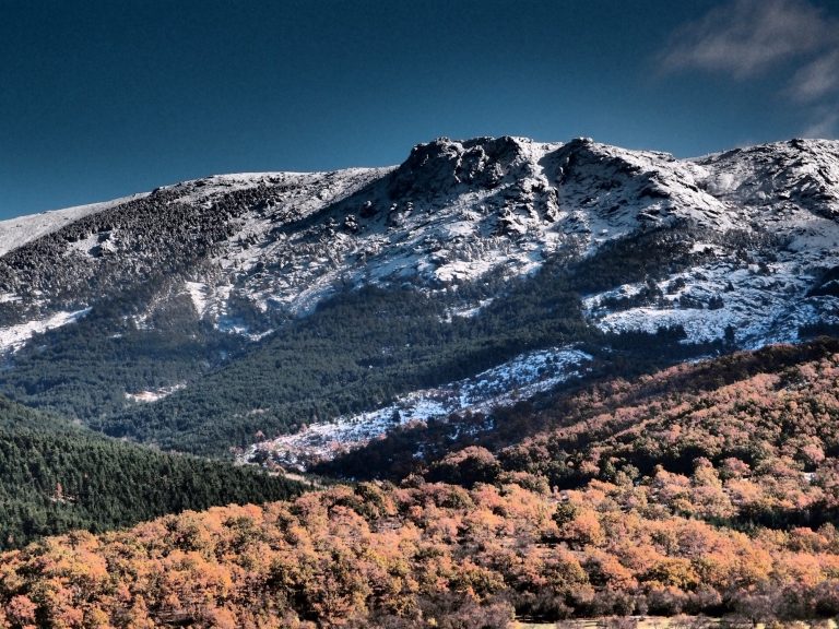 En la Sierra de Guadarrama: Parque Nacional y Natural Montañas nevadas con vegetación colorida en primer plano y cielo despejado al fondo.