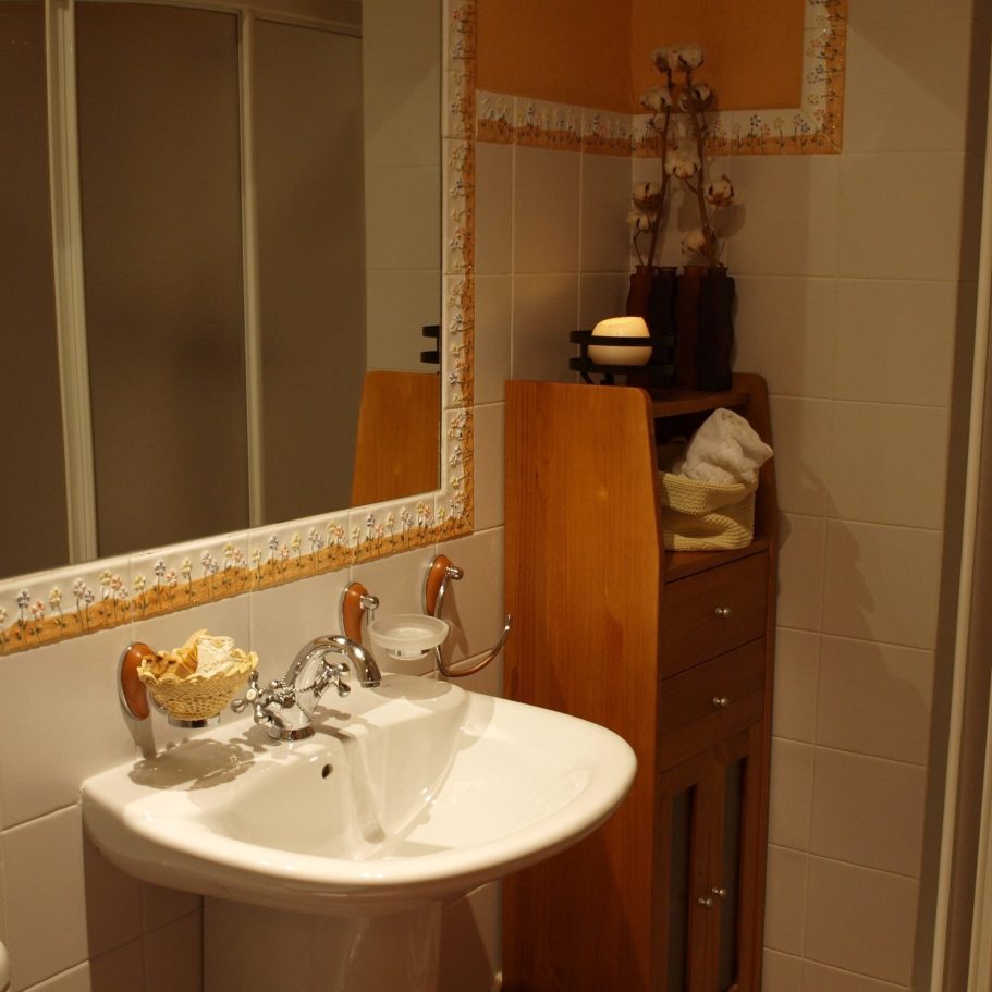 Baño rústico impecable con ducha y detalles de calidad en casa rural sostenible. Baño con lavabo, espejo, mueble de madera y decoración en tonos suaves.