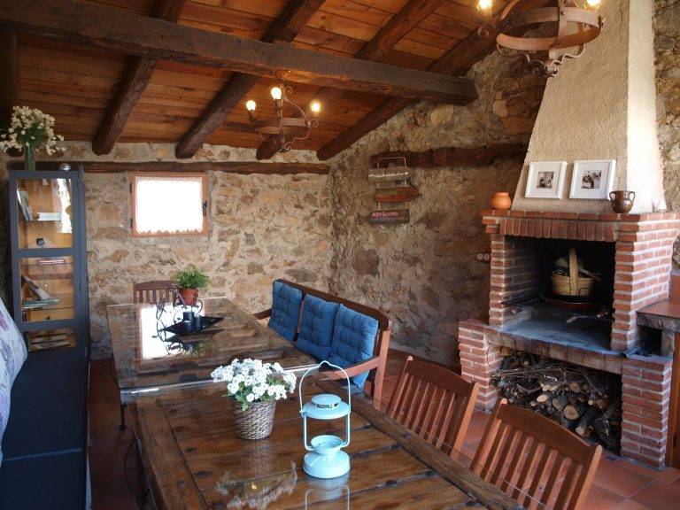 Barbacoa de obra en cenador cubierto independiente para uso exclusivo de huéspedes Interior de una cabaña rústica con mesa de madera, chimenea y decoración acogedora.