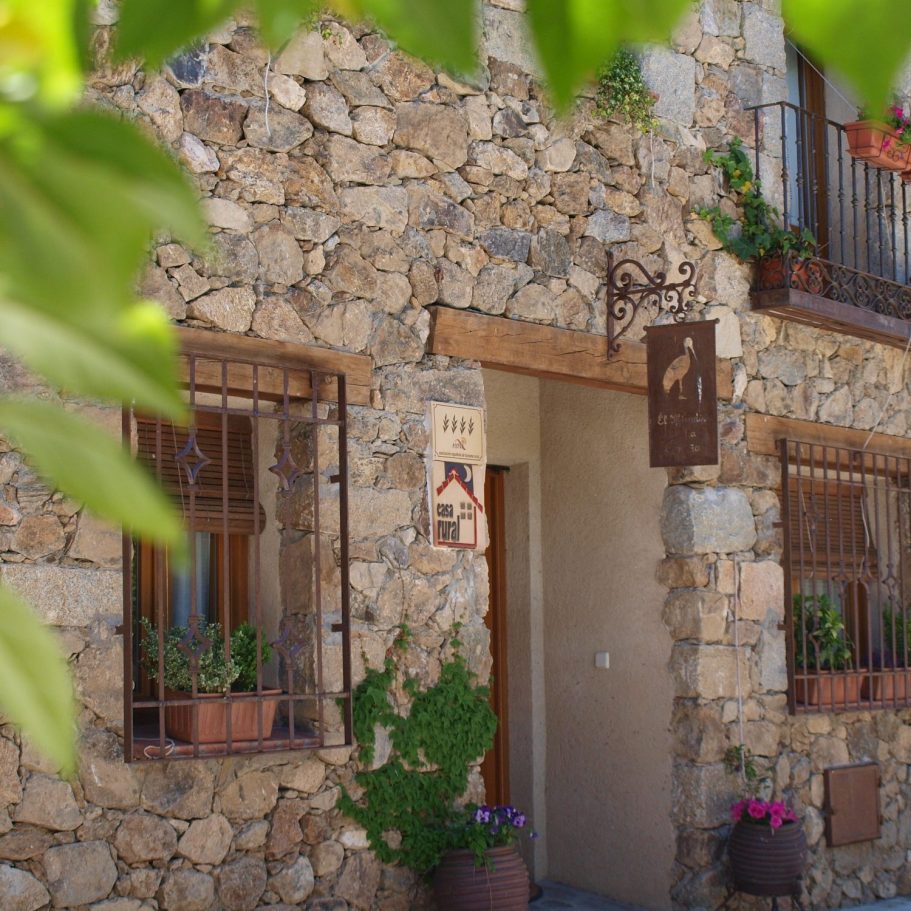 Casa rural El Mirador de la Cigüeña en Cabanillas del Monte Segovia cerca de La Granja Fachada de piedra con flores y ventanas en un entorno rural.